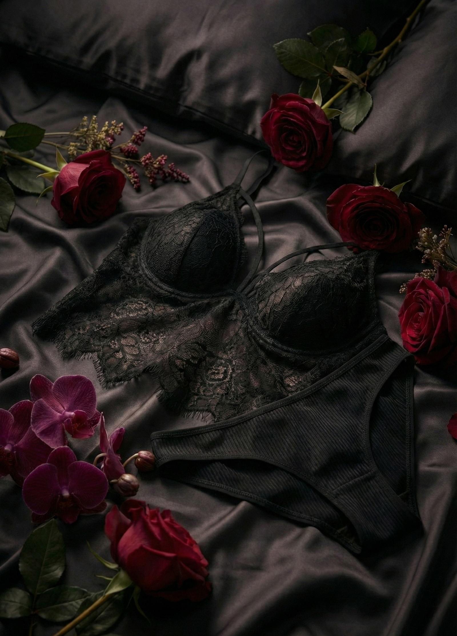 Black lace lingerie on a dark fabric background with red roses and purple orchids.